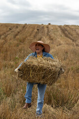 A smiling woman lifting a hay bale while working in the field in the Andes Mountains