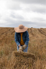 Naklejka na ściany i meble Unrecognizable woman wearing a sun hat putting on protective gloves to work lifting hay bales