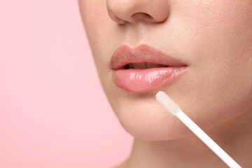 Woman applying lip gloss on pink background, closeup. Space for text - obrazy, fototapety, plakaty
