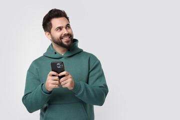 Happy young man using smartphone on white background, space for text