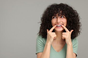 Young woman applying whitening strip on her teeth against grey background, space for text