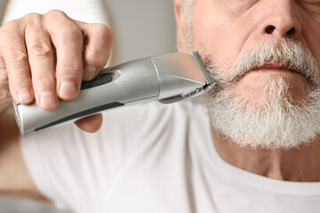 Man trimming beard with electric trimmer indoors, closeup - obrazy, fototapety, plakaty