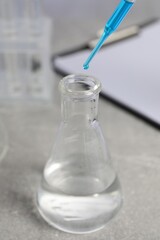 Laboratory analysis. Dripping liquid into flask on light grey table, closeup