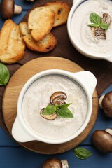 Delicious mushroom soup in ceramic pots and fresh ingredients on blue wooden table, flat lay