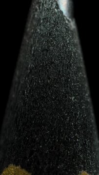 Vertical video. Black wooden pencil rotating on a black background. Slider. Macro. Sharp graphite tip.