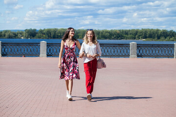 Two happy girlfriends teenagers are walking in the summer park.