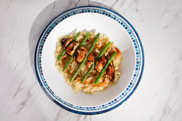 overhead view of barbeque chicken breast with asparagus and asian noodles in a white dish set on a blue plate on a marble tabletop