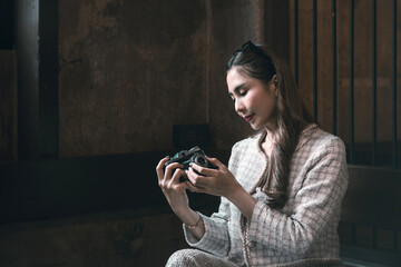 Beautiful young Asian brunette woman wearing fashion clothes casual dress and ancient camera. Portrait fashion model at traditional architecture old wall vintage building. Retro style.