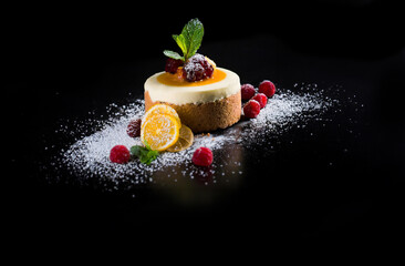 A cheesecake pastry with fruits and powdered sugar on a  black background.