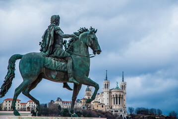 Fototapeta na wymiar Lyon, France - April 21 2013: Equestrian statue of Louis XIV on Place Bellecour with Basilica Notre Dame de Fourvière in background