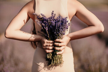 girl holding bouquet lavender flowers. The flowers are purple and the woman is wearing a tan top. Concept of calm and relaxation, as lavender is often associated with these feelings.