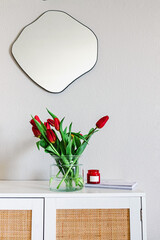 Minimalist living room with a fluid shape mirror on the wall and red tulips