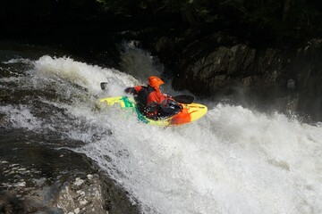 Kayaker in yellow green and orange boat with orange helmet paddling through rapids on Wells River...