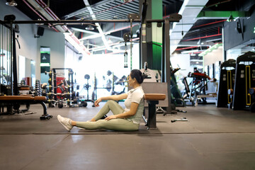 Asian woman exhausted and resting after doing exercise in modern gym room, rest time between sets. - obrazy, fototapety, plakaty