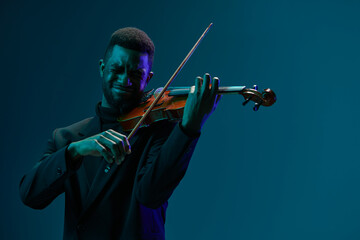 Elegant musician in black suit performing on violin against vibrant blue background on stage