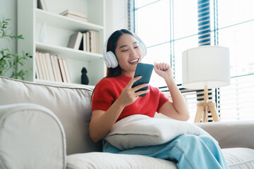 Young Asian woman relaxing on sofa at home, listening music with headset on cell phone. People lifestyle concept