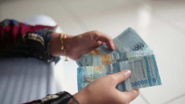 Woman counts many rupiah (IDR) Blue 50,000 banknotes in hands with blurred background. Indonesian paper currency