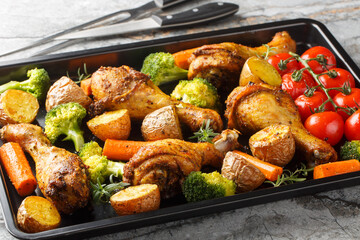 Tasty Baked ruddy chicken legs with potatoes, broccoli, tomato, carrot close-up on a baking sheet on the table. Horizontal