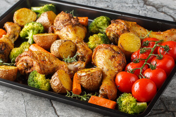 BBQ baked chicken drumsticks with seasonal vegetables and rosemary close-up on a baking sheet on...