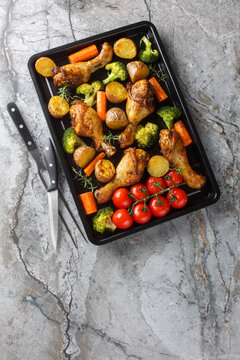 Homemade baked chicken drumsticks with vegetables and rosemary close-up on a baking sheet on the table. Vertical top view from above