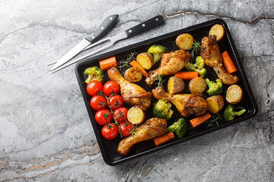 BBQ baked chicken drumsticks with seasonal vegetables and rosemary close-up on a baking sheet on the table. Horizontal top view from above