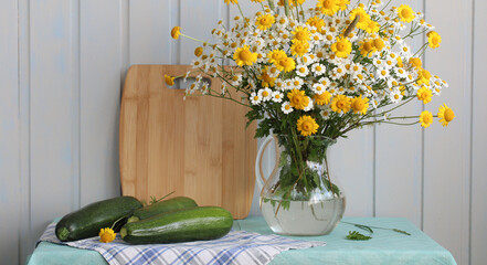 bouquet of yellow and white daisies in a jug and green zucchini on the table
