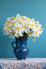 garden daffodils in a blue jug on a table with a lace tablecloth, spring flowers.