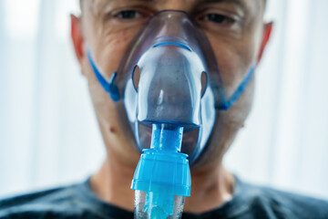 Close up view of unhealthy man wearing nebulizer mask in home. Health, medical equipment and people concept - obrazy, fototapety, plakaty