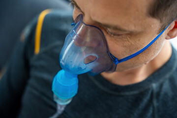 Unhealthy man wearing nebulizer mask in home. Health, medical equipment and people concept