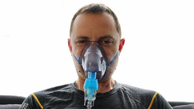 Unhealthy man wearing nebulizer mask breathing in home. Health, medical equipment and people concept.