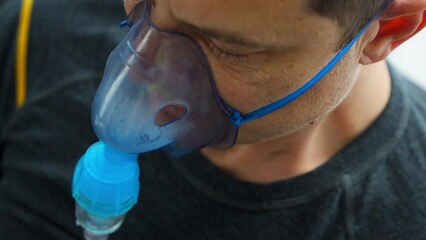 Unhealthy man wearing nebulizer mask breathing in home. Health, medical equipment and people concept. - Powered by Adobe