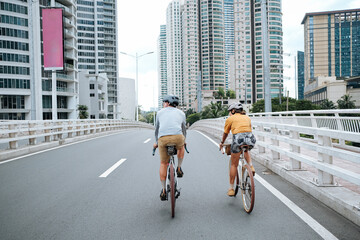 A couple is cycling in the city, crossing a bridge during summer time.