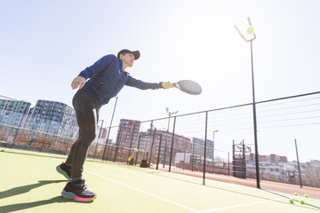 A girl in sportswear is training on a paddle tennis court. The girl is hitting the ball against the...