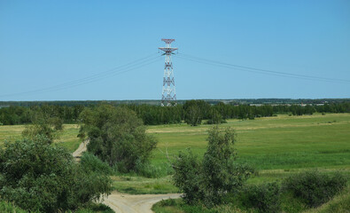 Obraz premium High voltage power lines leading through a green field. Transmission of electricity by means of supports through agricultural areas.