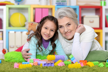 Cute girl and grandmother playing with colorful plastic blocks