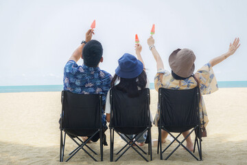 Parent and children celebreate summer by eating icecream.Happy family sitting in chairs on the beach