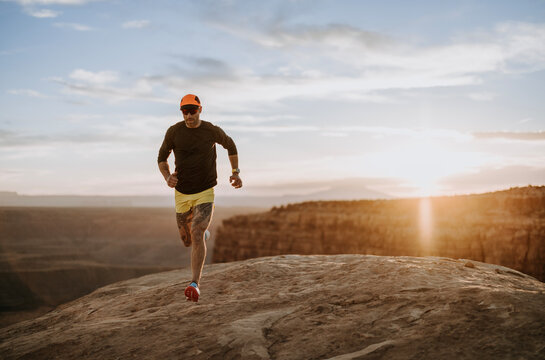 Man with leg tattoos runs along rocks at sunset in Utah desert