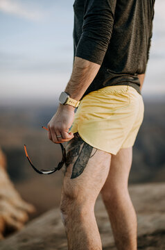 runner with leg tattoos and watch holds sunglasses