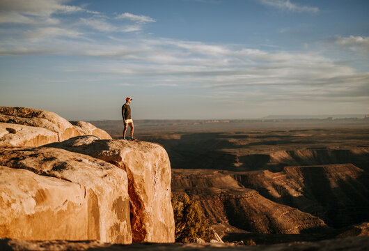 Man in shorts stands at edge of cliff overlooking San Jaun River, Utah