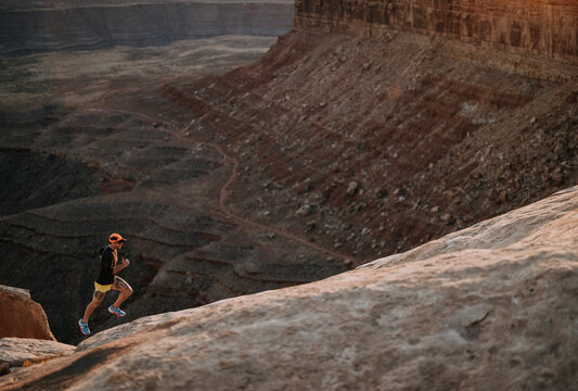 Male jogger sprints up hill along edge of cliff, Mexican Hat, Utah