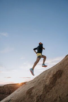 Male trail runner leaps and bounds up rocky incline, Utah
