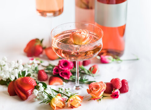 Mini rose floats in coupe glass of rose wine, with flowers and b