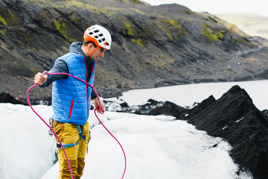 Young man in colourful clothes swings a rope on an Icelandic glacer