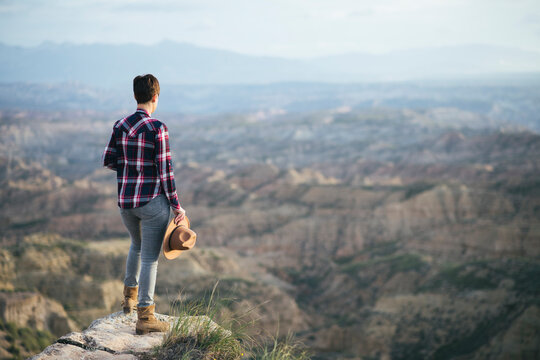 Woman in a plaid shirt and hat looking at the landscape from above.