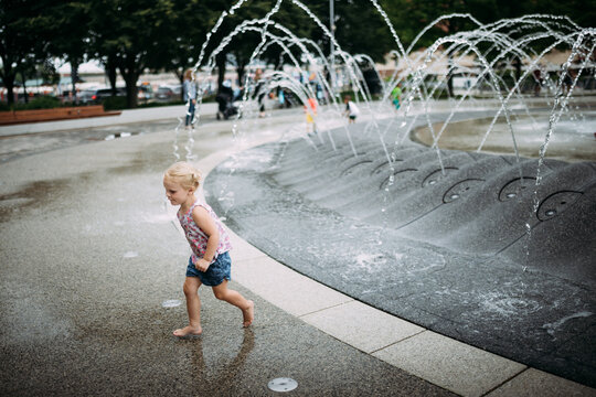 Young child running through city fountain during summer