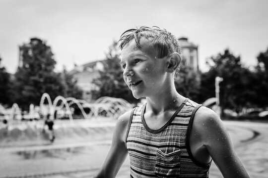 Child covered in water drops at city fountain during summer