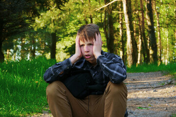 Fototapeta premium The boy holds his head in his hands and is feeling stressed.