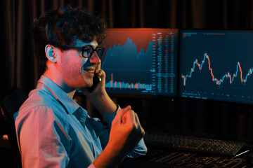 Successful business trader calling to broker, raising fist up with highest profit on global market online in real time at neon light modern office. Concept of stock exchange young businessman. Gusher.