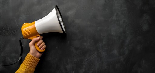 A hand in a mustard yellow sweater holding a megaphone against a textured black background, signaling a call to attention or announcement.