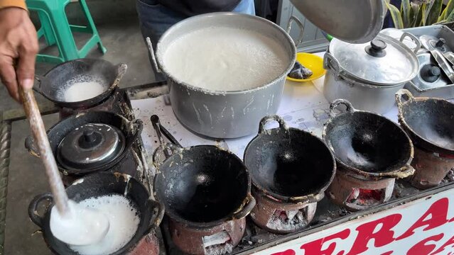 The process of making traditional dessert named Serabi made from rice flour and coconut milk by an old man with charcoal stove